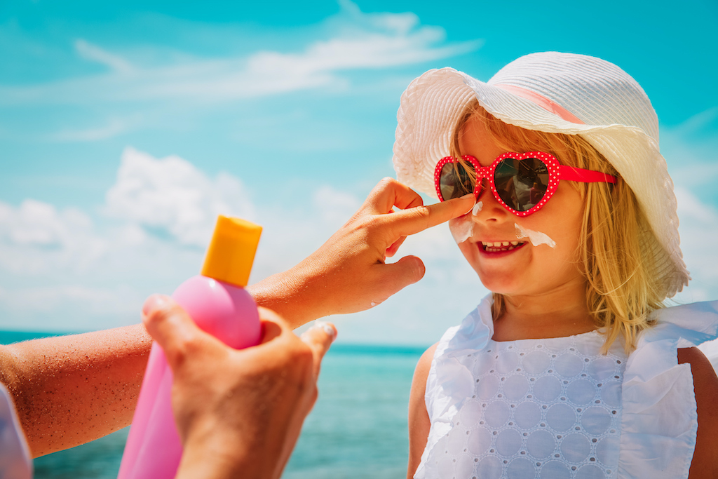 mother put sunblock cream on little daughter face at beach