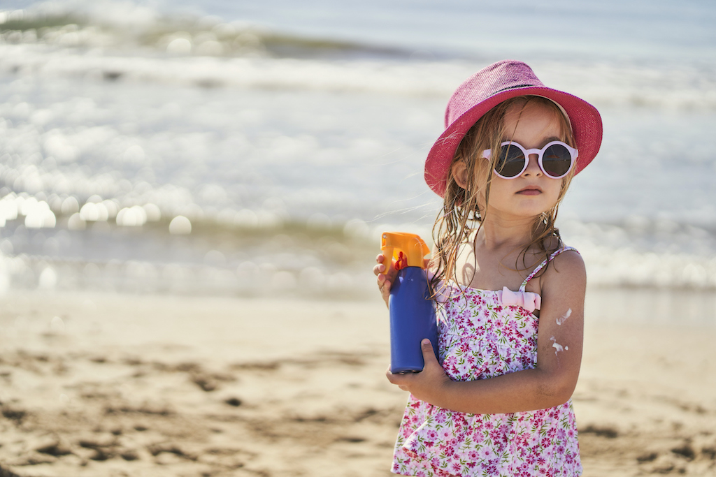 portrait of a girl with a bottle of sunscreen on the beach