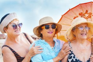 Group of women friends aged smiling and posing for a photo in summer outdoor leisure activity together in friendship. Coloruful accessories and sunglasses. Holiday vacation elderly people females lady